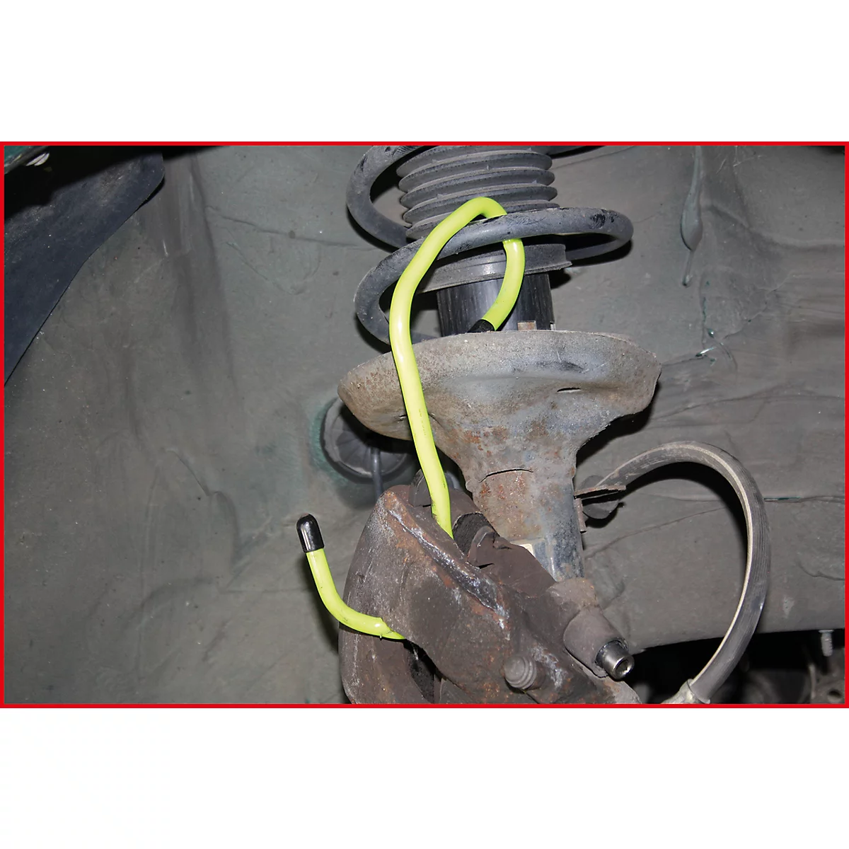 Nahaufnahme der Fahrzeugfederung. Gelbe Schlauchleitung gewickelt um Federbein. Rostige Metallteile dominieren.